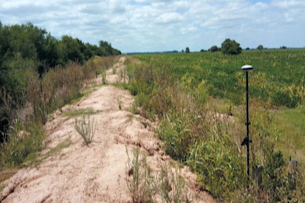 GPS surveying equipment on a dirt mound beside a field of crops.