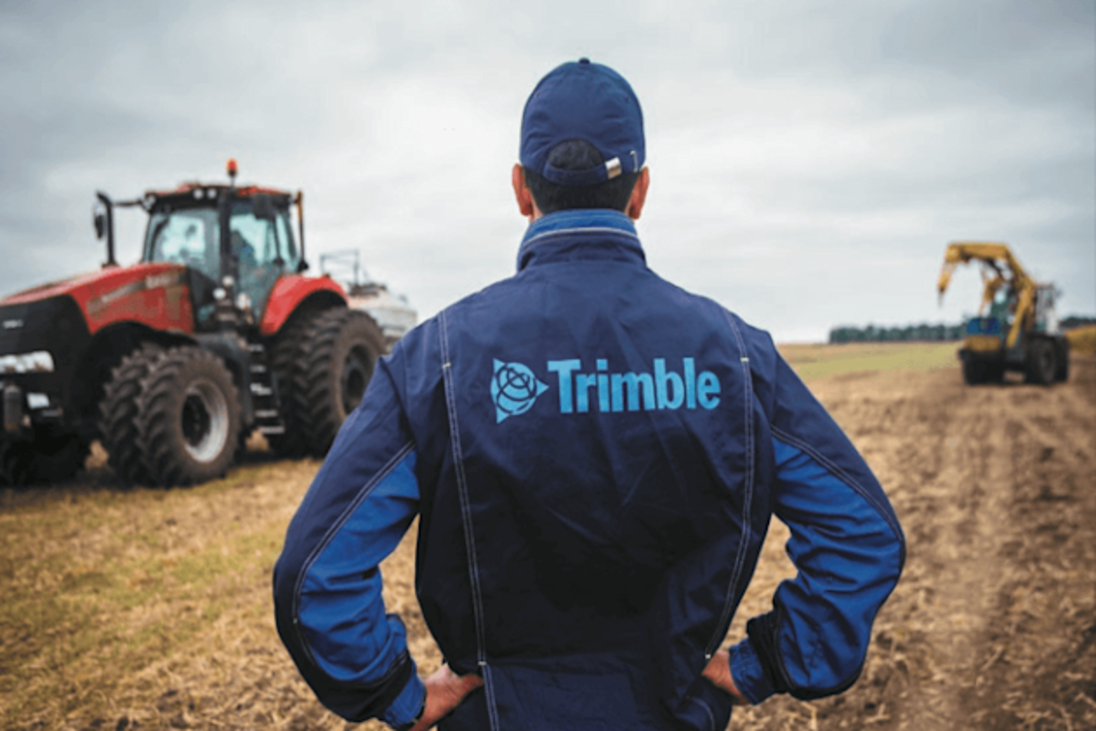 Farmer in a Trimble jacket looks out over a field with tractors.
