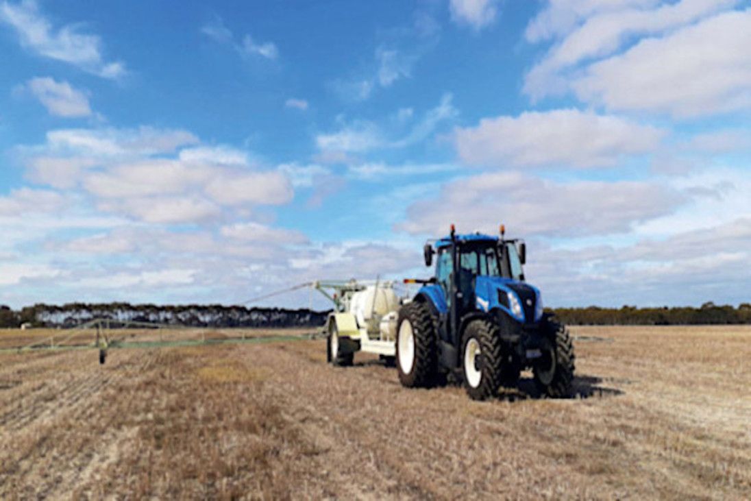 Blue tractor spraying a field under a partly cloudy sky.