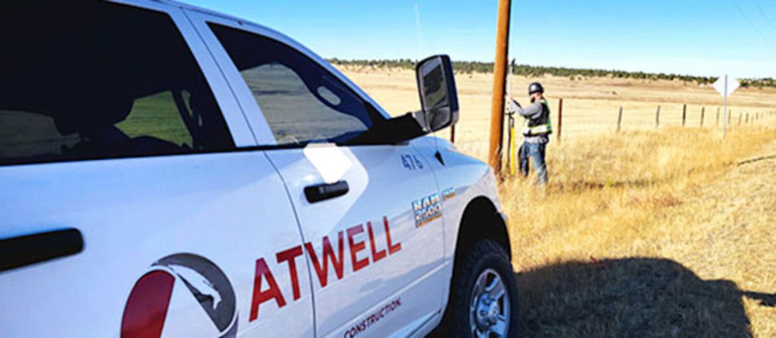 White Atwell Construction truck with a worker in the background near a utility pole.